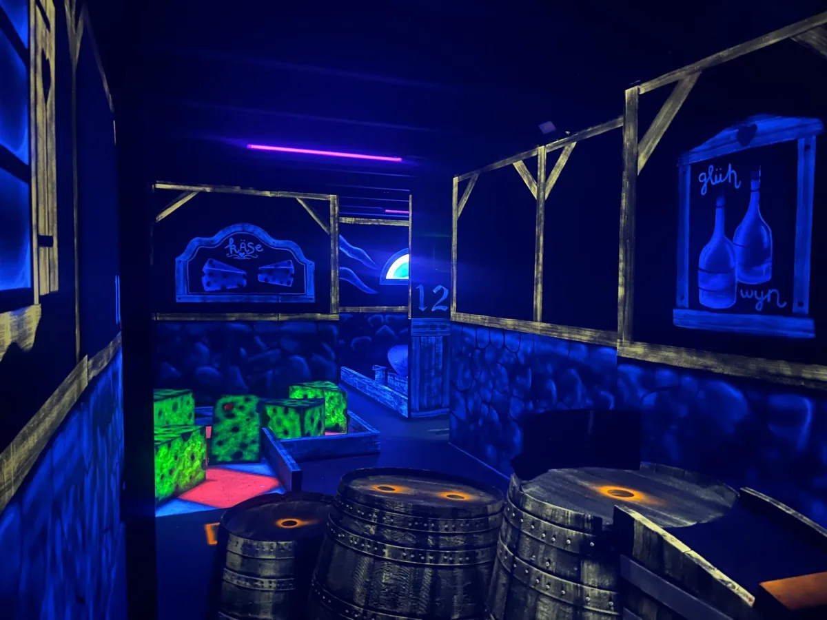 Indoor Playgolf bij Playdôme Roosendaal: holes tussen kaasblokken en houten tonnen in Alpijnse sfeer onder blacklight