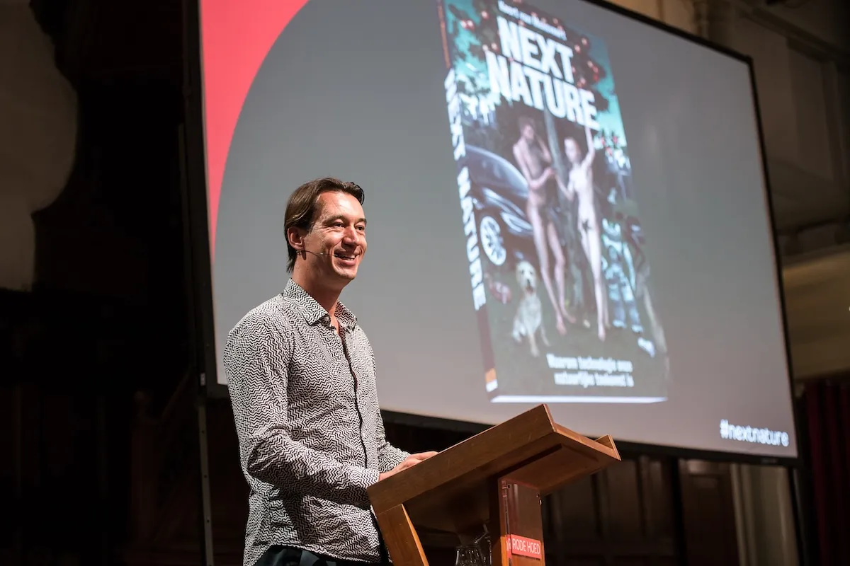 Koert van Mensvoort speaking at a lectern in front of a screen showing the book Next Nature